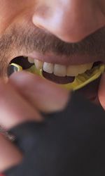 Man with athletic gloves putting in a mouthguard
