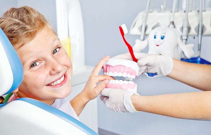 Smiling girl in dental chair with model teeth