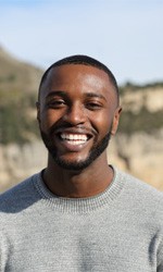 Man in grey shirt smiling in front of a large cliff