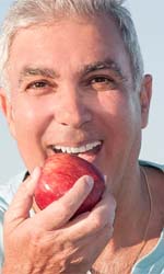 man happily eating an apple because he invested in implant dentures in Studio City