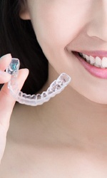 A woman holding an aligner and a mold of a mouth with traditional braces