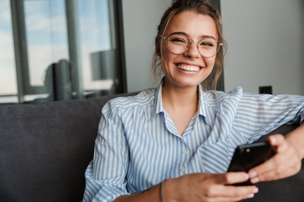 Woman with glasses smiling while sitting on couch