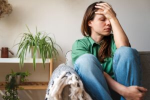 Woman sitting on her sofa, suffering from migraine pain 